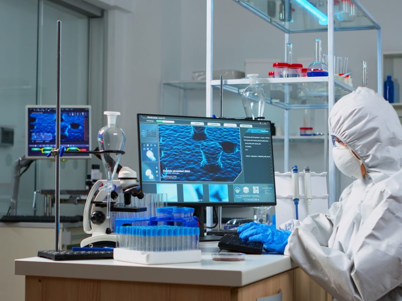 Doctor in ppe suit looking at blood sample in test tube sitting in equipped lab. Scientist working with various bacteria and tissue, concept of pharmaceutical research for antibiotics against covid19